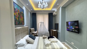 Een moderne hotelkamer met een groot bed, een televisie, een kroonluchter en een schilderij aan de muur.