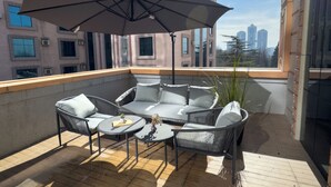 Een terras op het dak met buitenmeubilair, waaronder een bank en stoelen, en een grote parasol.