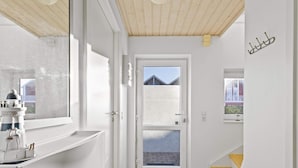 A narrow hallway with a wooden ceiling, a white door leading outside, and a small window with a view of a building. - 5 Star Holiday Home in Lokken (Lokken)