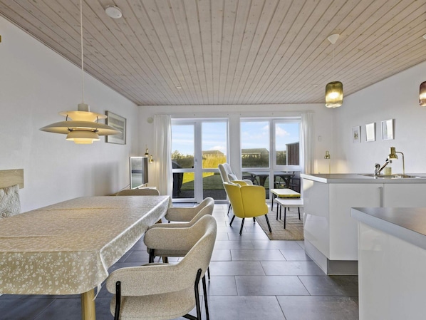A modern kitchen with a dining area, large windows, and a view of the outdoors.