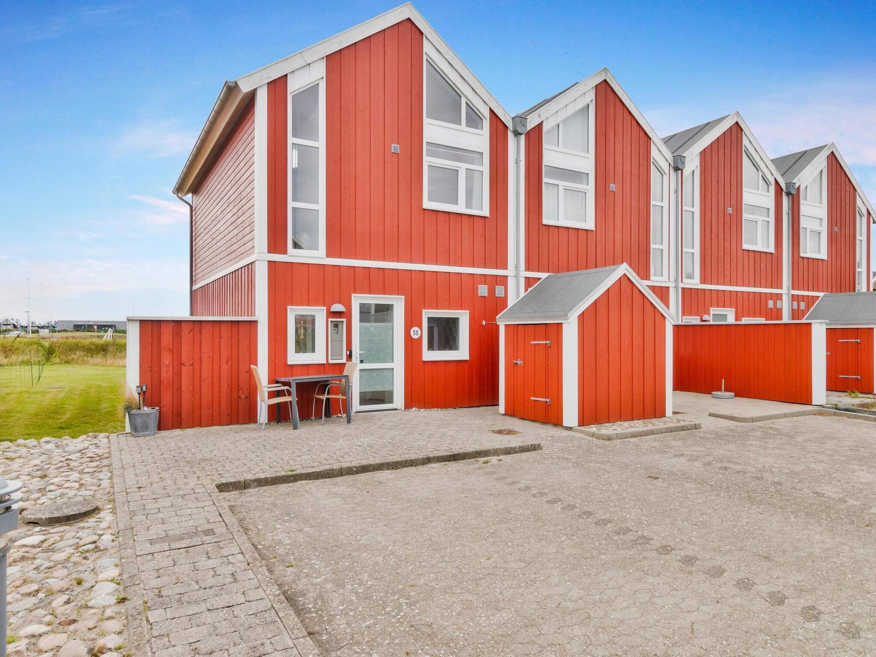 Un bâtiment rouge doté de nombreuses fenêtres et portes, une allée pavée et un petit espace extérieur aménagé pour s’asseoir.