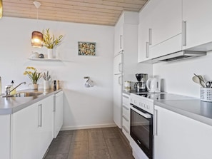 A modern kitchen with white cabinetry, a stainless steel countertop, a coffee maker, and a stove.