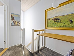 A hallway with a wooden bench, a framed painting of a field with cows, and a poster on the wall. - 5 Star Holiday Home in Lokken (Lokken)