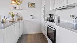 A modern kitchen with white cabinets, a stainless steel countertop, a coffee maker, and a kettle. - 5 Star Holiday Home in Lokken (Lokken)