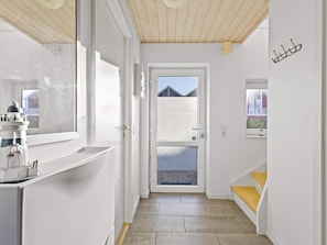 A narrow hallway with a wooden ceiling, a white door leading outside, and a small window with a view of a building.