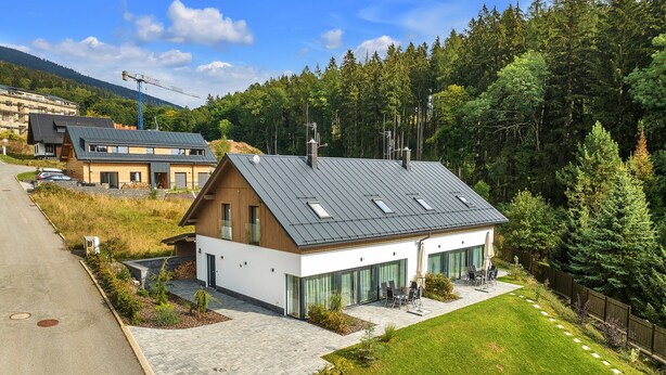 A modern house with a sloped roof, large windows, and a paved patio area. - Villa in Cerny Dul Near Ski Resort (Cerny Dul)