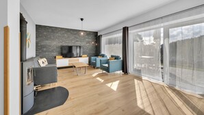 A modern living room with a stone wall, a flat-screen TV, a sofa, and a dining area. - Villa in Cerny Dul Near Ski Resort (Cerny Dul)
