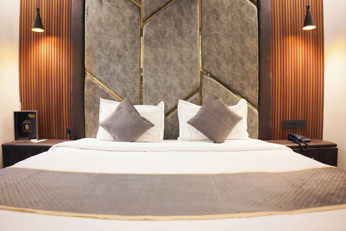 Una cama bien hecha con una colcha acolchada, dos almohadas y una mesita de noche con una lámpara y un teléfono.