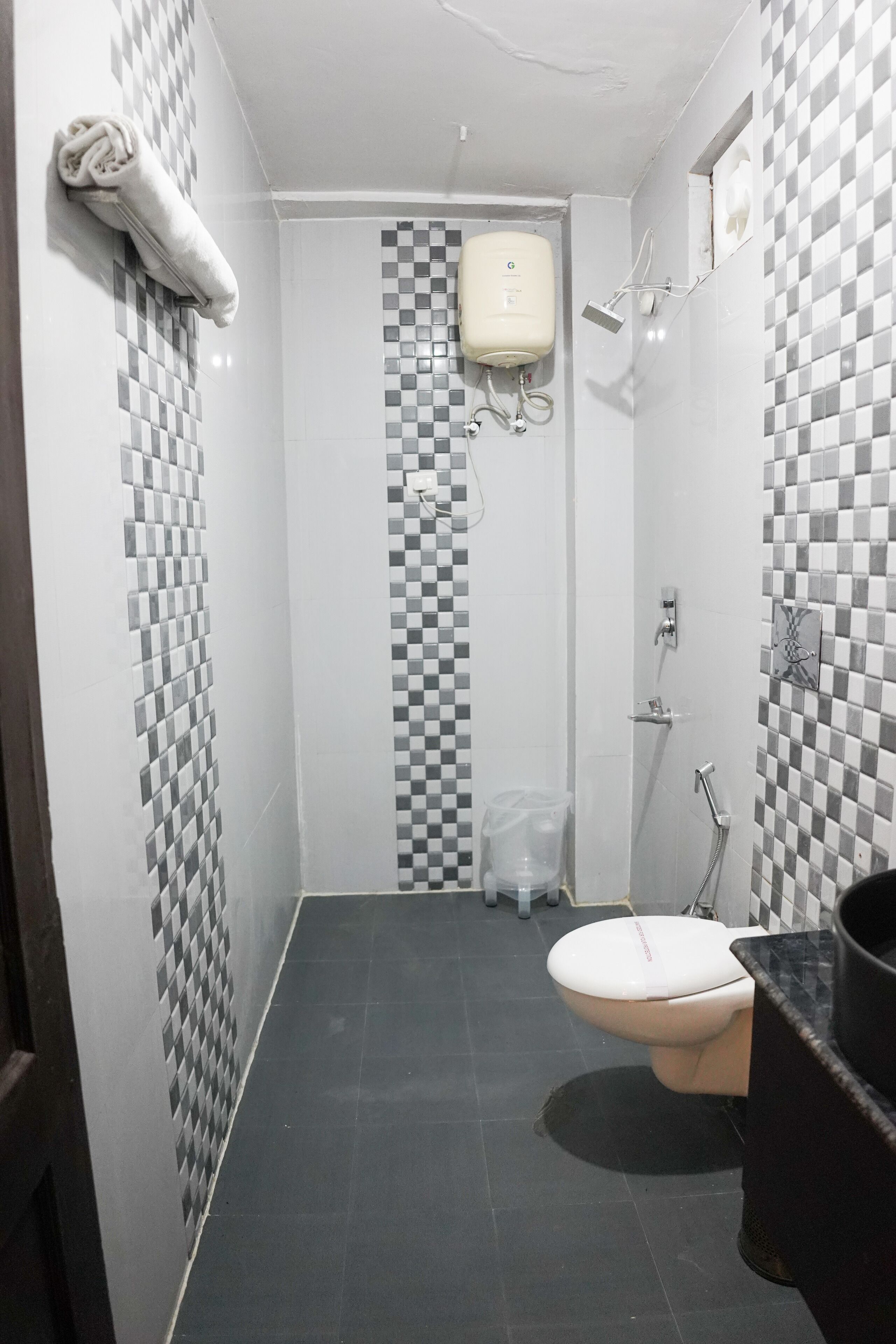 Un baño con piso a cuadros, un inodoro, una ducha y un perchero para toallas.