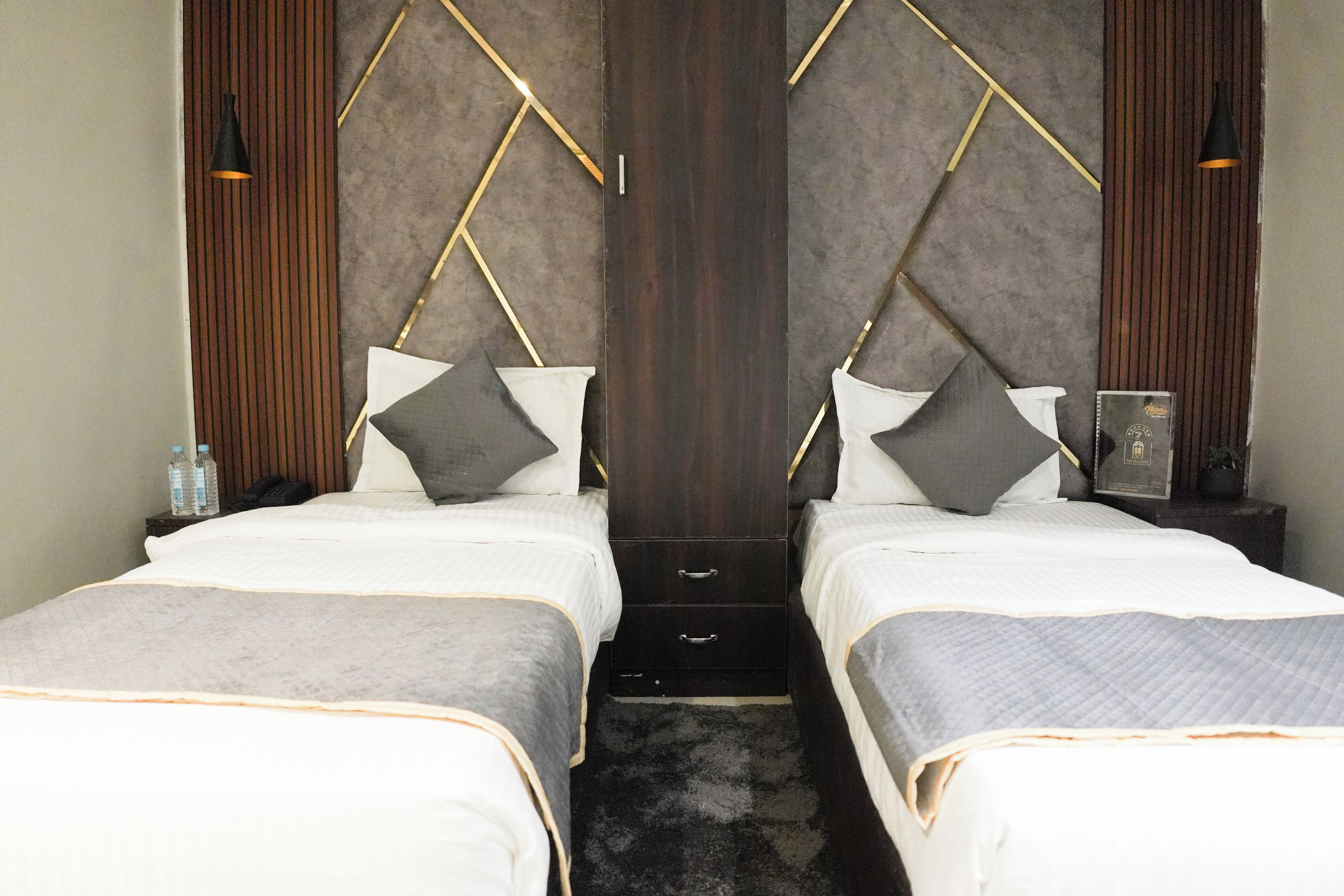 A hotel room with two beds, a dark wood headboard, and a small bedside table with a lamp.