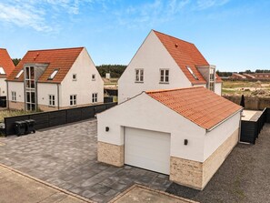 A row of modern houses with red-tiled roofs and white walls, featuring a central garage and a paved driveway.