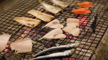Various fish being grilled on a metal grate over an open flame.