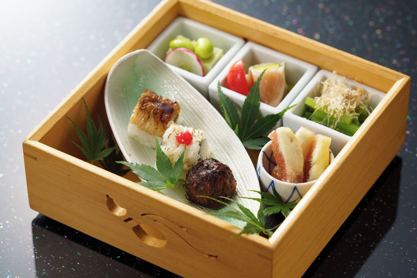 A wooden box containing various food items, including sushi, pickled vegetables, and a bowl of rice.