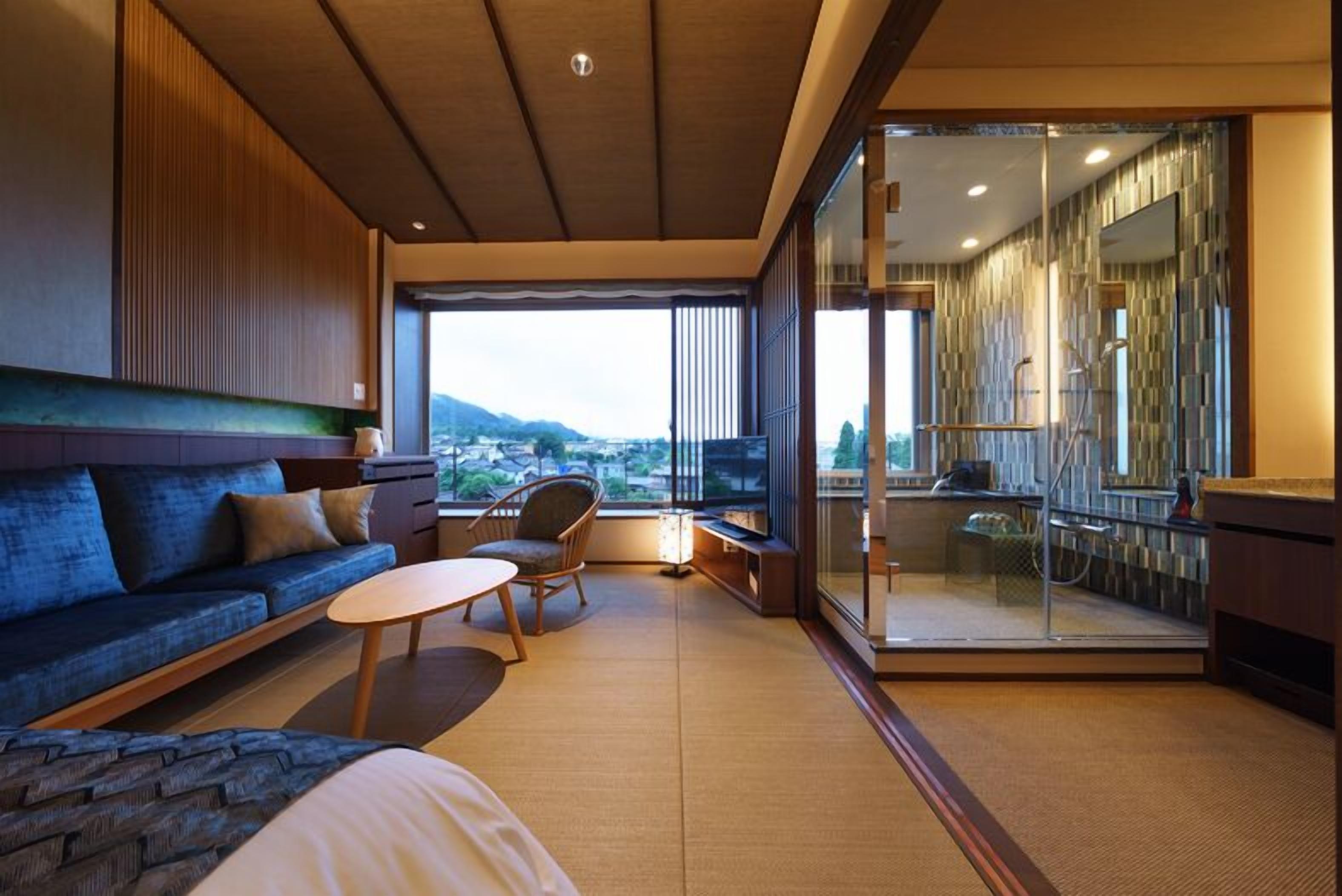 A modern hotel room with a sofa, a small table, a chair, a bed, and a balcony with a view.