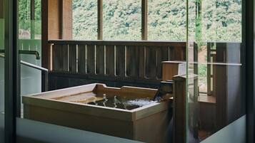 A wooden bathtub with a wooden bench, a glass railing, and a view of trees through the window.