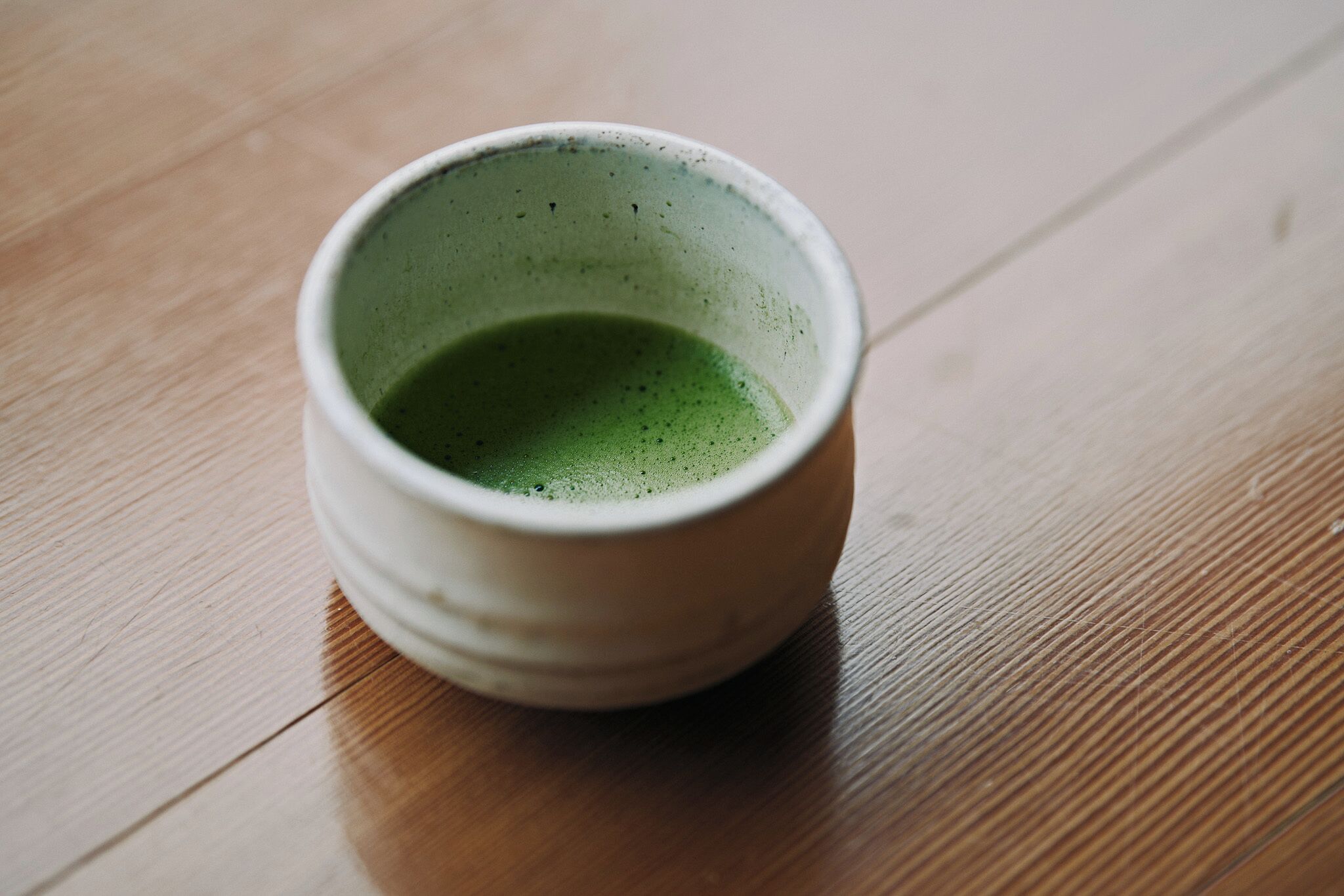 Una taza de cerámica blanca con contenido verde sobre una superficie de madera.