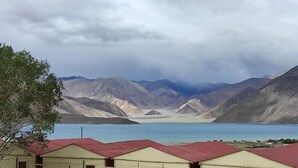 A mountainous landscape with a lake and a row of buildings with red roofs. - Ecstasy Huts Pangong (Leh)