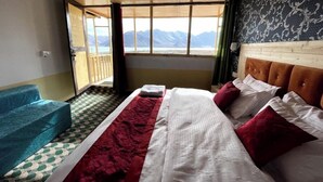 A room with a bed, a blue sofa, and a view of mountains through a large window. - Ecstasy Huts Pangong (Leh)