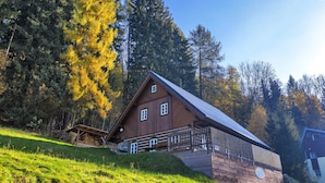 Una baita di legno con tetto spiovente, un portico e un muro in pietra.