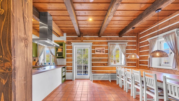 Interno di una baita in legno con cucina, zona pranzo e un'ampia finestra.