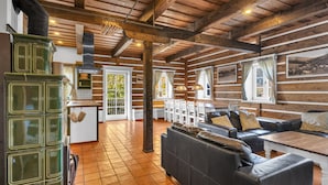 Un interno rustico con travi in legno, una stufa verde, un divano in pelle nera e un pavimento piastrellato.