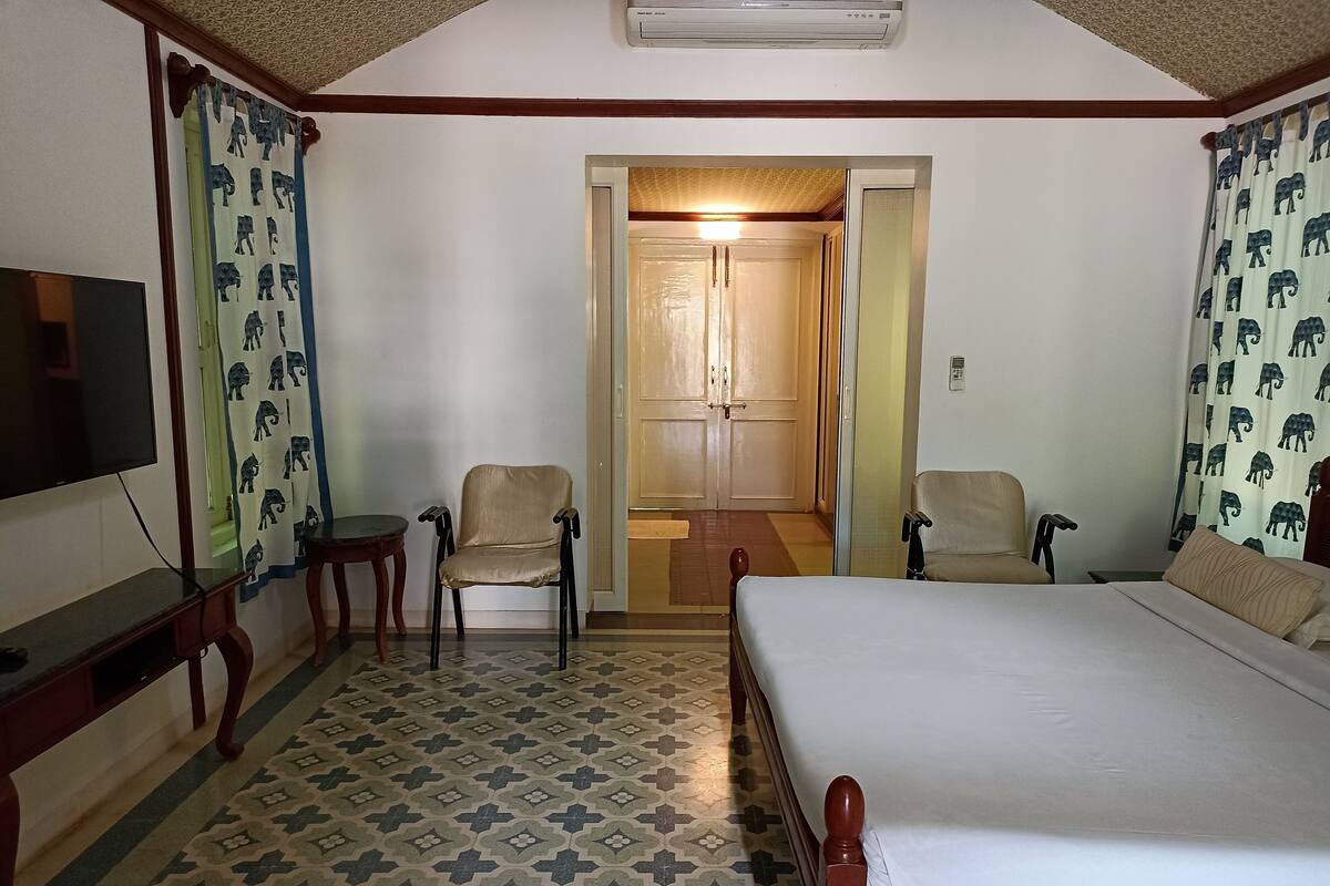 Quarto de hotel com cama, duas cadeiras, televisão e cortinas estampadas.
