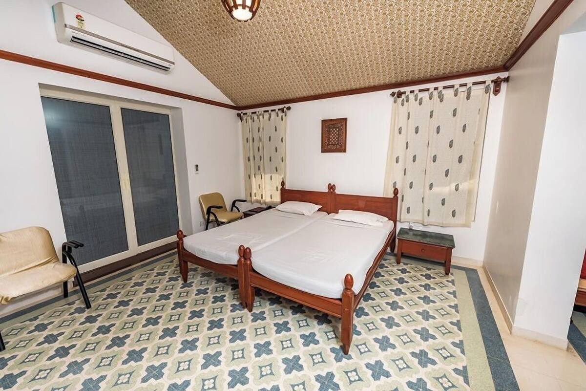 Quarto com cama grande, uma cadeira, ar condicionado e janela com cortinas.