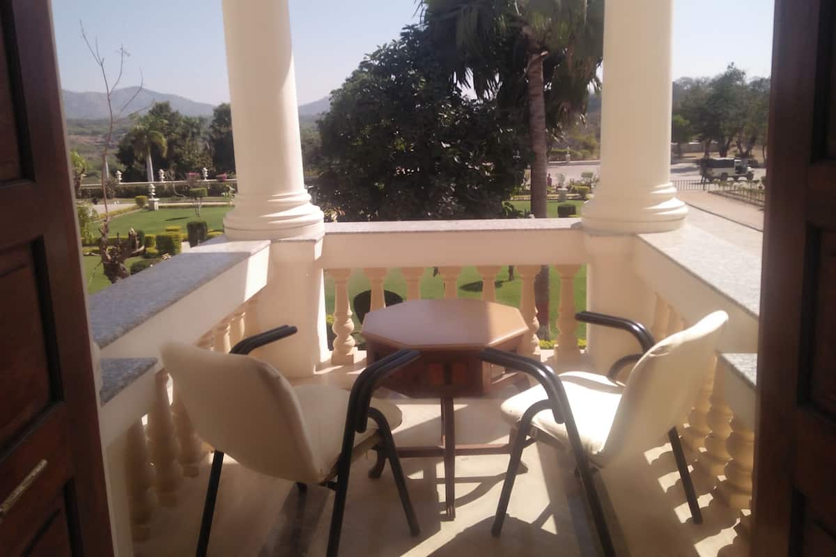 Varanda com mesa e cadeiras, com vista para um jardim ajardinado e palmeiras.