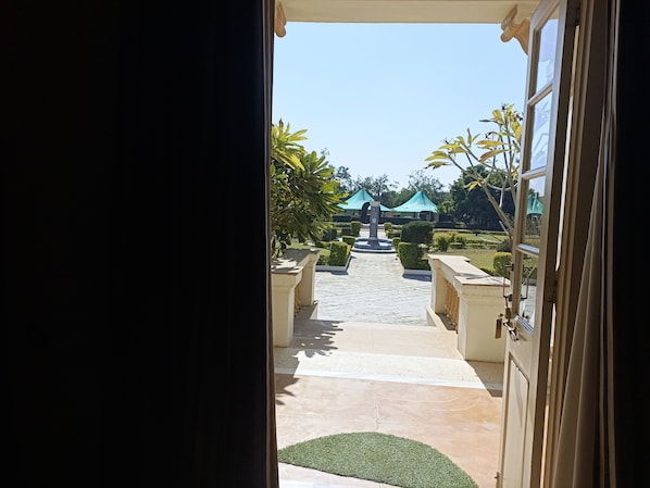 An open door leading to a courtyard with a tiled pathway, potted plants, and a central fountain. - Balaram Palace Resort (Palanpur)