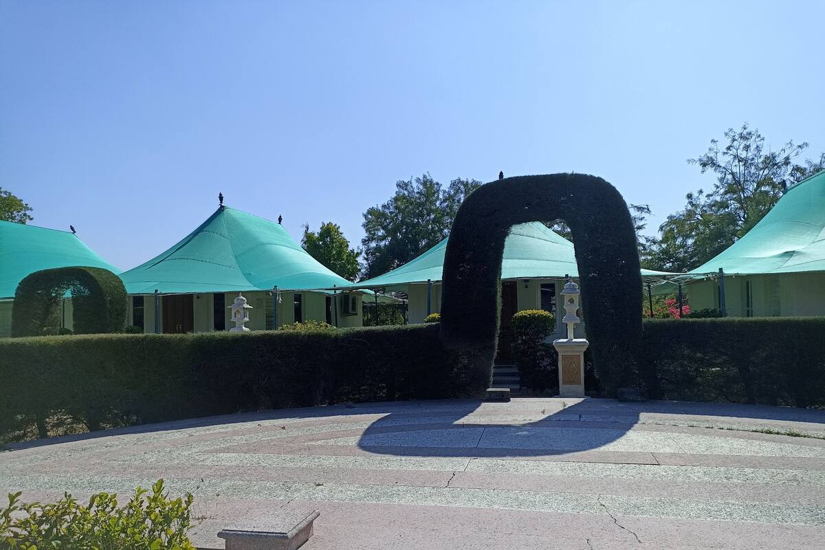 Um pátio com um arco central, cercado por edifícios com telhados verdes e sebes bem cuidadas.