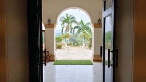 Een open deur die uitkomt op een binnentuin met palmbomen en een betegelde vloer.