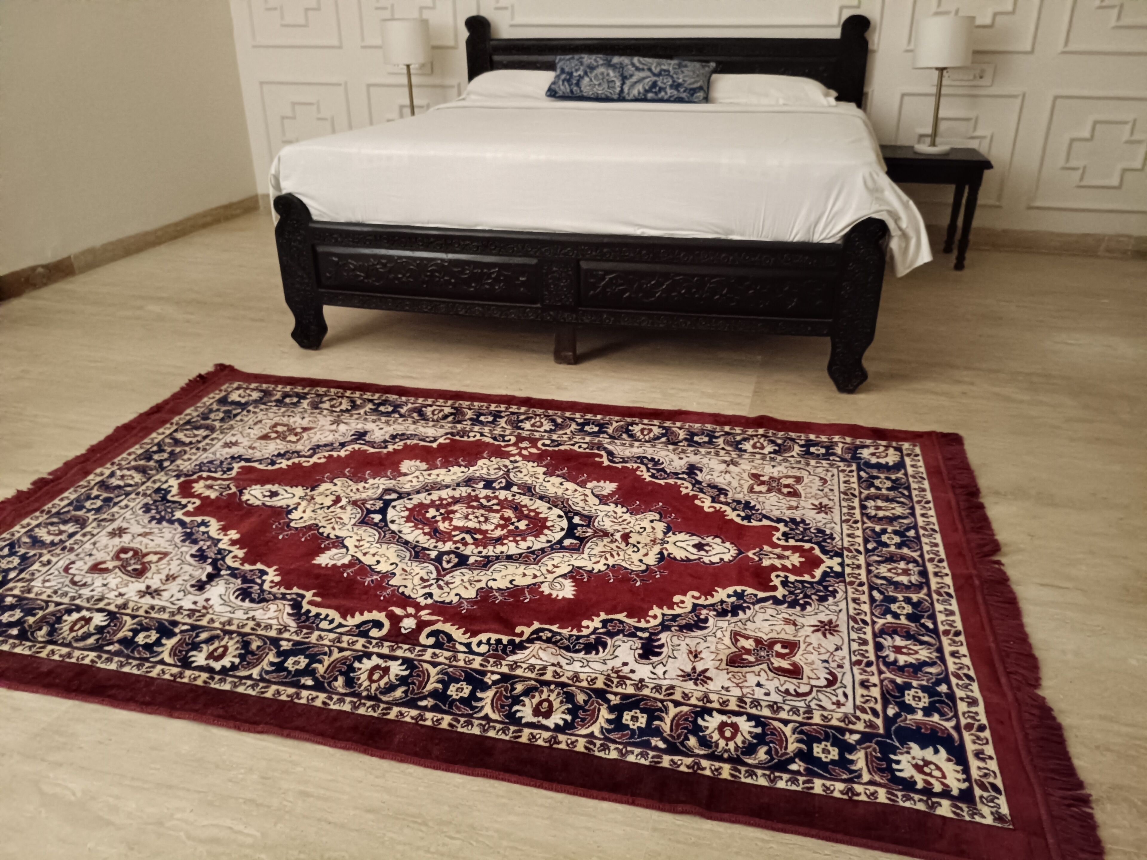 A bed with a white bedspread, a dark wooden headboard, and a patterned rug in front.