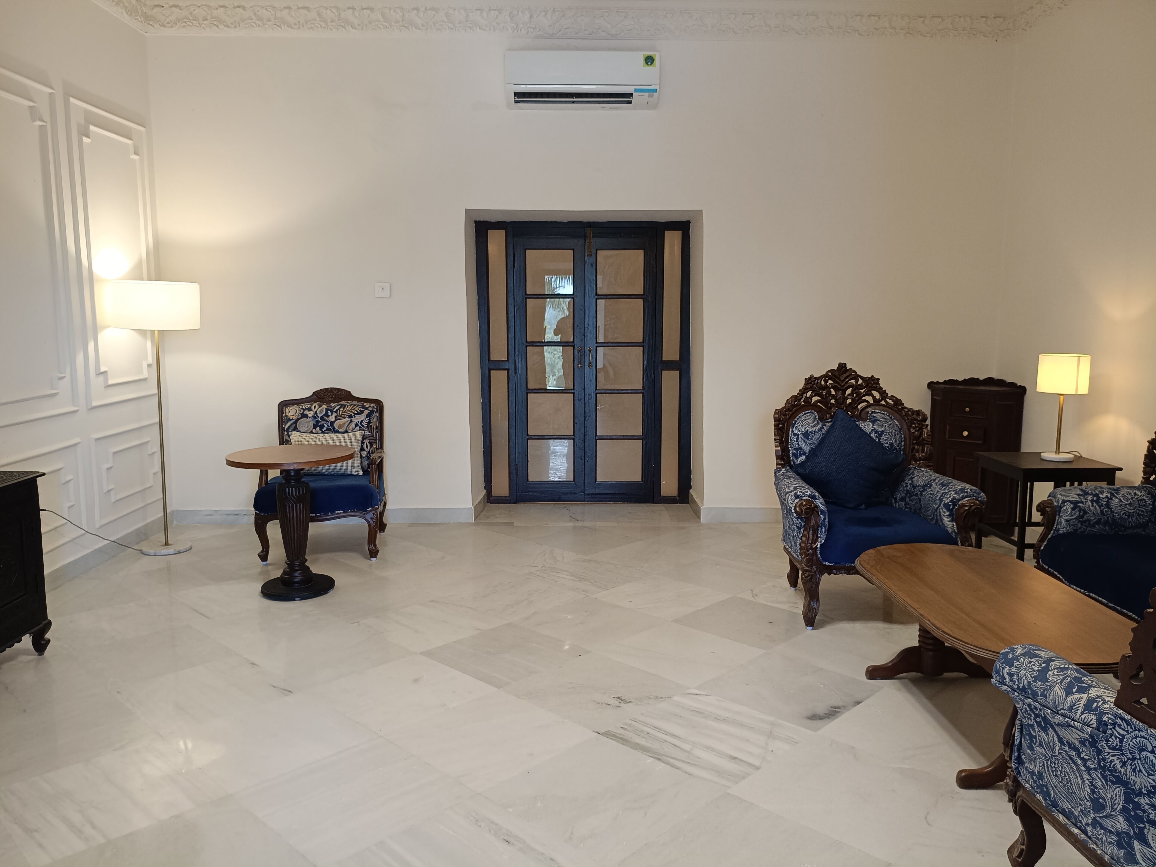 Una habitación con un sofá estampado, una mesa de centro de madera, una lámpara y una puerta con panel de vidrio.