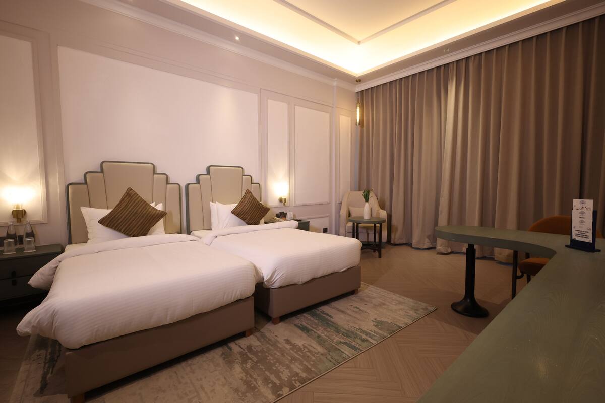 Une chambre d’hôtel avec deux lits, un coin salon avec une table et une grande fenêtre avec des rideaux.