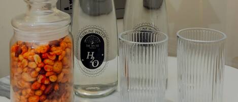 A marble countertop with a glass jar filled with nuts, two bottles of water, and two clear glasses.