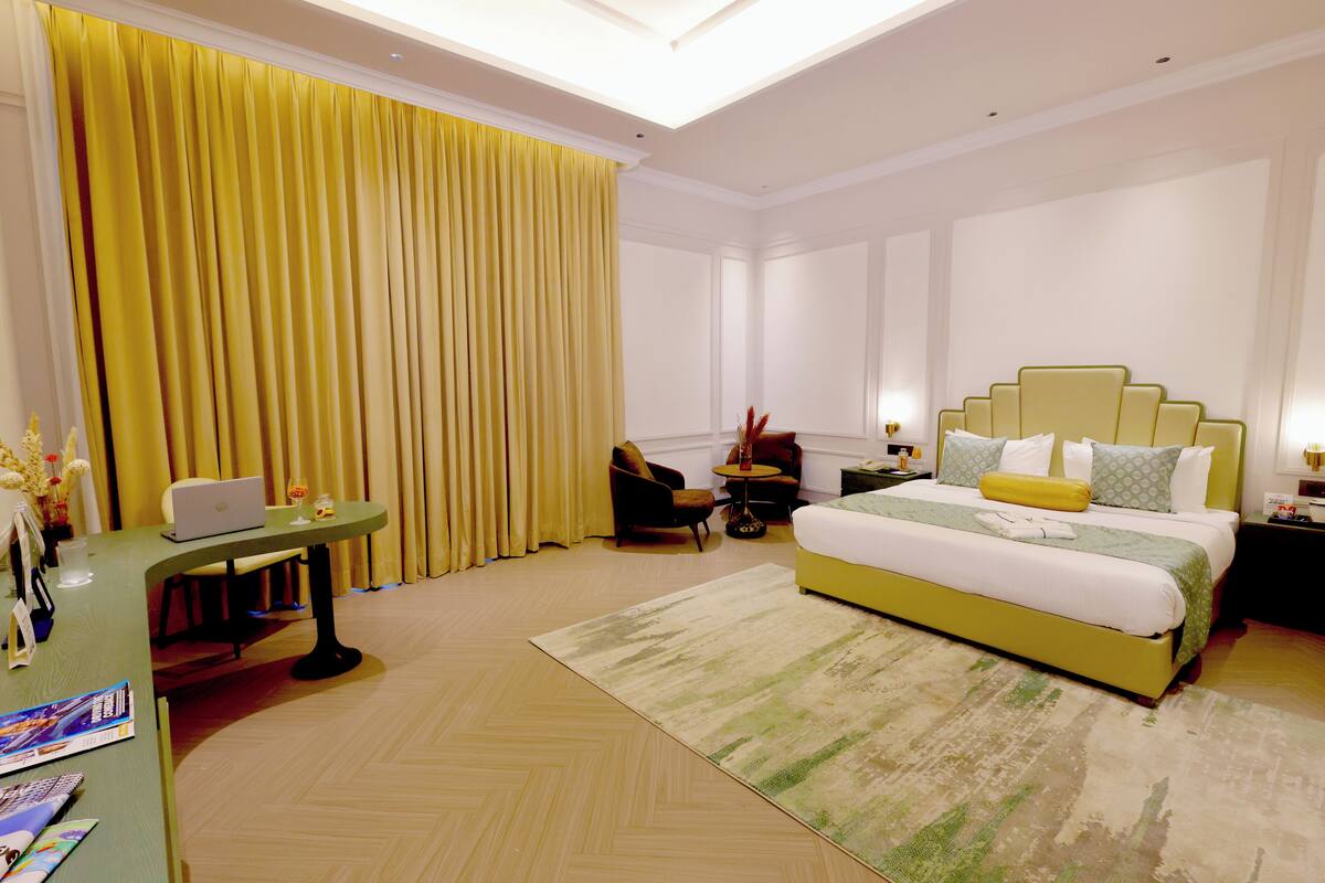 Une chambre d’hôtel avec un lit, un bureau, une chaise, une lampe et une fenêtre avec des rideaux.