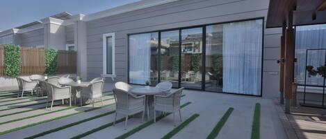 A modern outdoor patio with a dining area, a wooden fence, and a large sliding glass door.