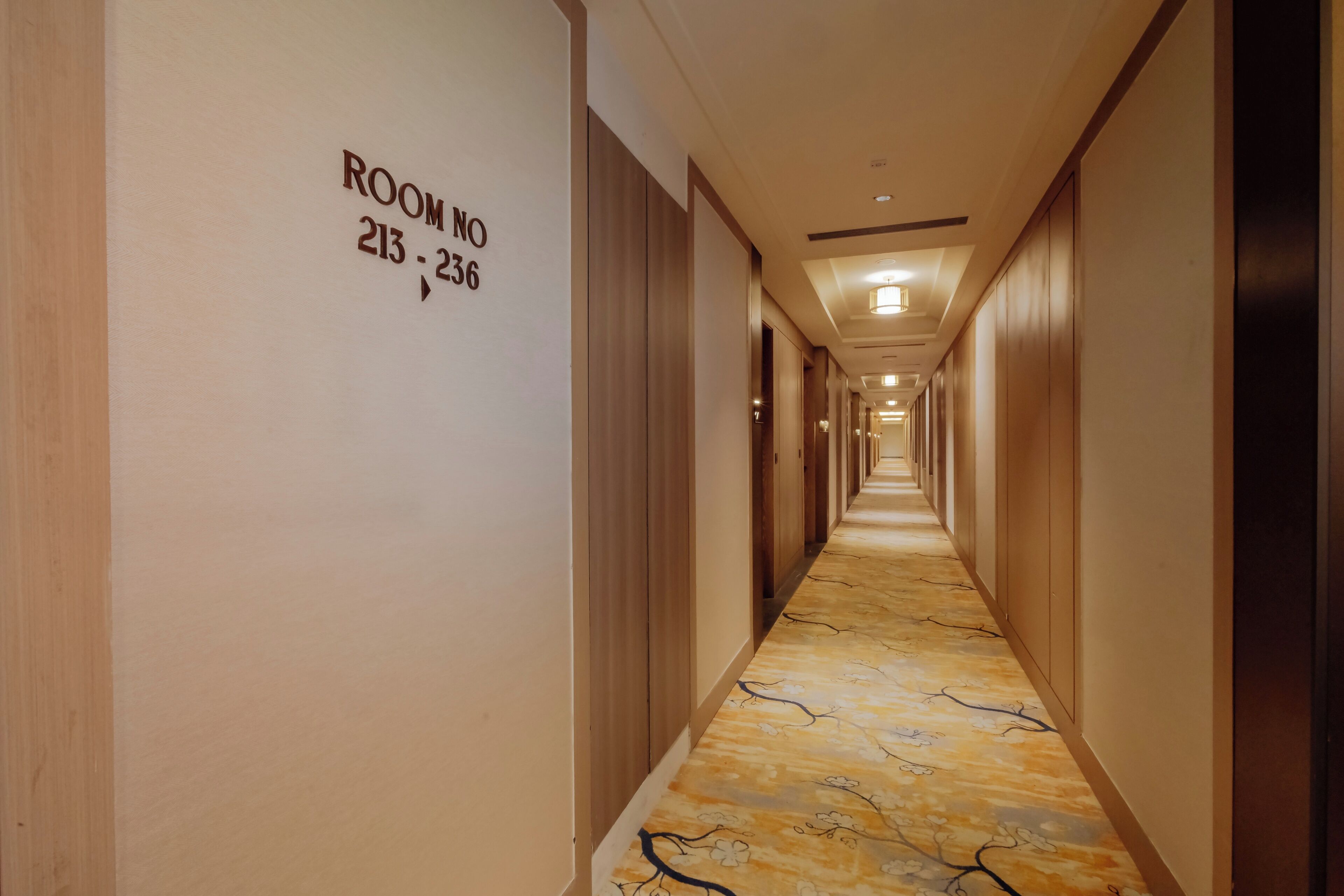 Un couloir d’hôtel avec un sol en marbre et des murs en bois. Les numéros de chambre 213 à 236 sont visibles sur le mur de gauche.