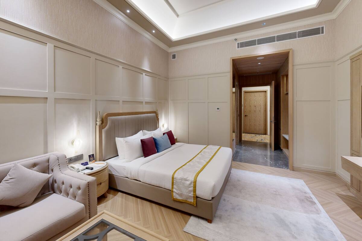 Une chambre d’hôtel moderne dotée d’un grand lit, d’un coin salon avec un canapé et un fauteuil, d’une table de chevet avec une lampe et d’un téléviseur.