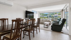 A modern living room with a dining area, a flat-screen TV, and a view of a residential area.