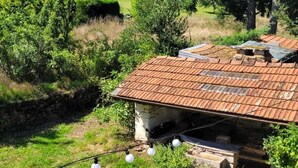 A rustic stone house with a tiled roof, surrounded by lush greenery and a clear blue sky.