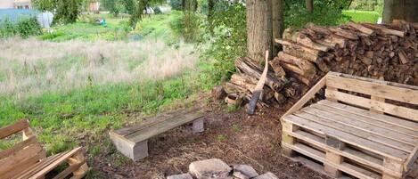 Un espacio de descanso al aire libre de estilo rústico, con un brasero de piedra, bancos de madera y un montón de leña.