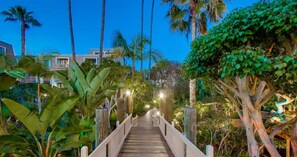 Stroll through the lush garden, surrounded by tropical plants and trees, along a winding pathway with a simple white railing.