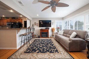 A modern kitchen with a built-in microwave, a large flat-screen TV, and a dining area with bar stools. - Walk to the Beach! Private Backyard and Fire Pit (Oceanside)