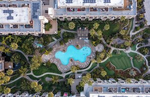 Vue aérienne d’un hôtel composé de plusieurs bâtiments, avec une piscine centrale et de nombreux espaces verts environnants.