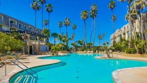 Una piscina d'hotel amb palmeres, gandules i un edifici amb balcons.