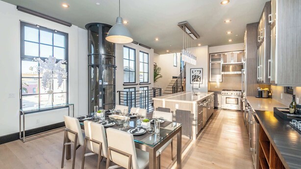 Una cocina moderna con electrodomésticos de acero inoxidable, un comedor con mesa de vidrio y una escalera que sube a un nivel superior.