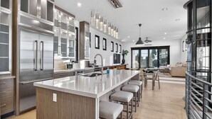 Una cocina moderna con una isla central, electrodomésticos de acero inoxidable y un comedor con taburetes de bar.
