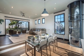 Uma sala de estar espaçosa com uma mesa de jantar posta para seis pessoas, um sofá grande e um elevador de vidro.