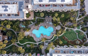 Vue aérienne d’un hôtel composé de plusieurs bâtiments, avec une piscine centrale et de nombreux espaces verts environnants.